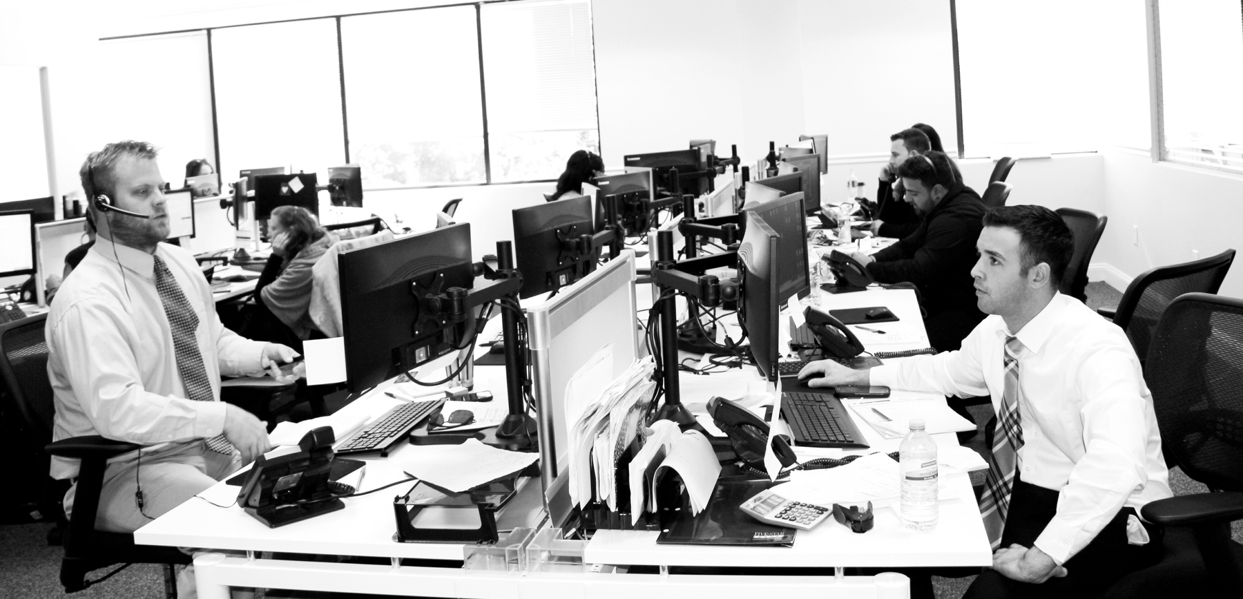 Les évaluations génèrent du stress chez les employés. Des hommes stressés en complet-cravate de part et d'autre d'une rangée d'ordinateurs sur la table commune d'un open space.
