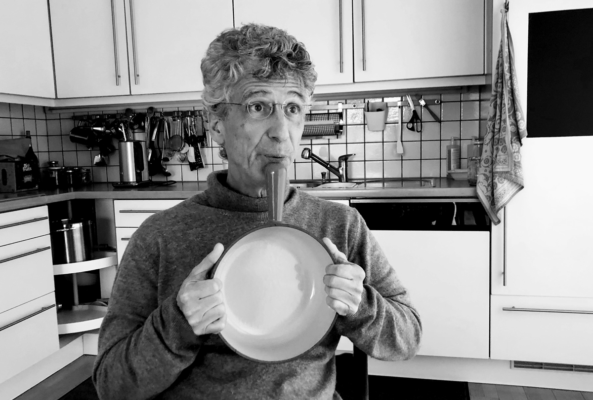 Portrait de Jean Duperrex dans sa cuisine avec le manche d'un caquelon comme flÃ»te indienne.